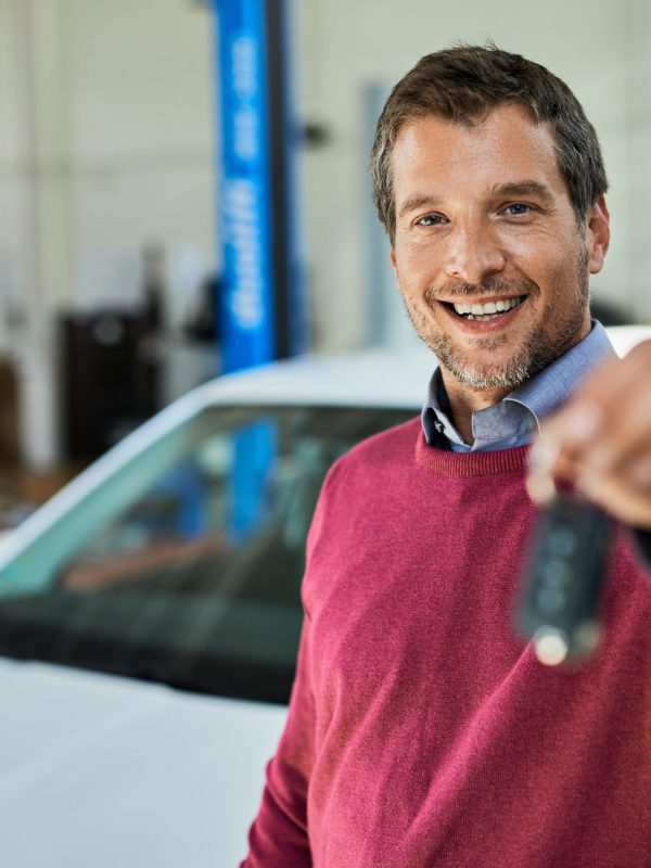 Satisfied male customer holding car key in auto repair shop and looking at camera.